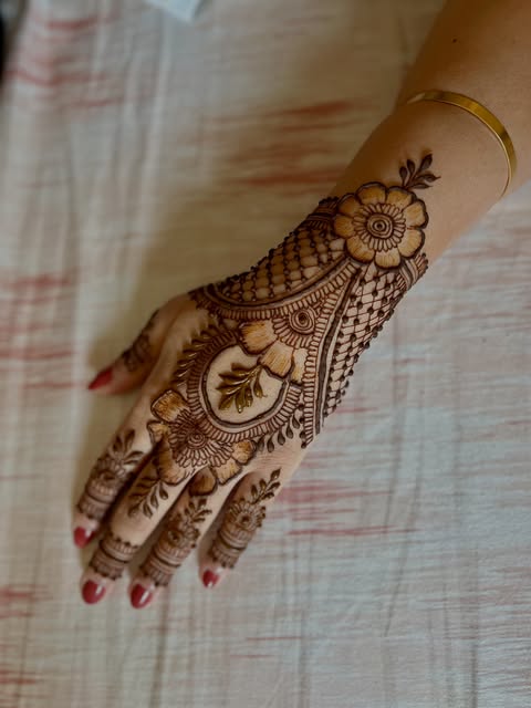 Arabic mandala henna on the back of a hand, finished beside a gold bangle