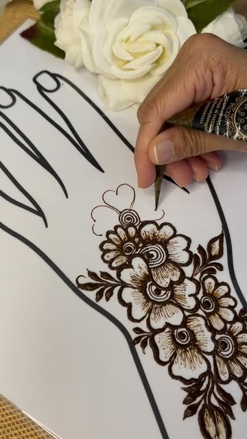 A floral henna design being drawn freehand on a practice sheet