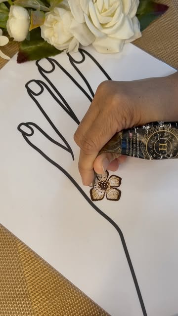 A hand-rolled organic henna cone drawing a flower motif on a practice sheet